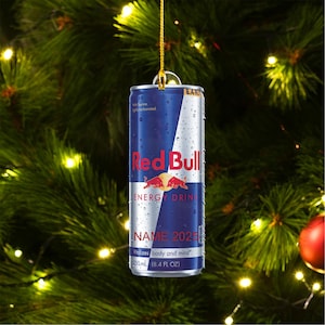 May include: A Red Bull energy drink can Christmas ornament. The can is blue and silver with the Red Bull logo and text. The ornament includes the text "NAME 2023" and "Vitalizes body and mind." The can is 250ml (8.4 fl oz).