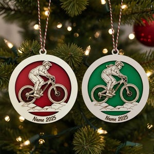 May include: Two round Christmas ornaments with a mountain biker design. One ornament has a red background, the other green. Both have a white border and a mountain biker silhouette. The text "Name 2025" is printed on the bottom.
