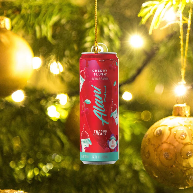 Puede incluir: Una lata roja de bebida energ&eacute;tica Alani Nu Cherry Slush, colgada como adorno en un &aacute;rbol de Navidad. La lata presenta el texto "Cherry Slush" y "Energy". La lata es de 355 ml.