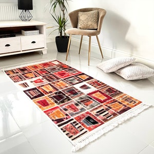 May include: A colourful, geometric patterned rug with a white background and fringe edges. The rug is laid out on a white tiled floor.