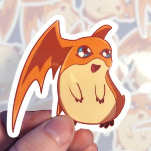 May include: A sticker of a cartoon orange and yellow dragon with blue eyes and a wide open mouth. The dragon has small wings and is standing on two legs.