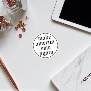 May include: A white circle sticker with black text that reads "make america emo again" in a gothic font.