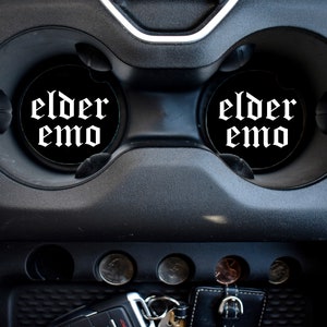 May include: Two black car cup holders with white "elder emo" text in a gothic font.