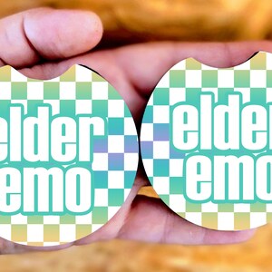May include: Two round coasters with a checkered pattern in white and light blue. The coasters have the text "elder emo" in white letters on a green background.