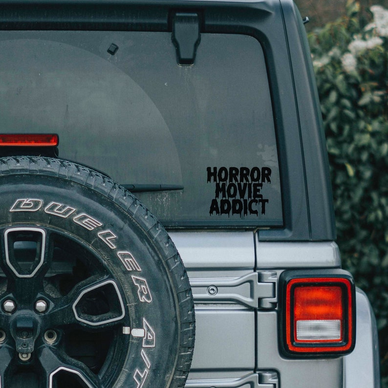 May include: A black and silver car with a sticker on the back window that says "Horror Movie Addict".