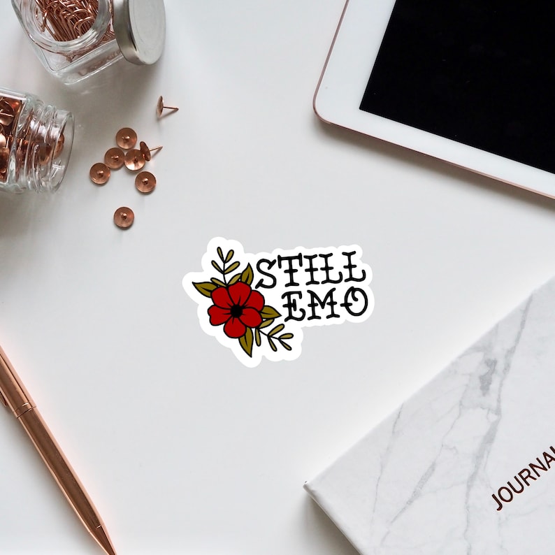 May include: A sticker with a red flower and green leaves with the text "STILL EMO" in black.