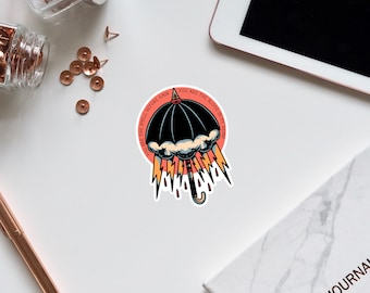 May include: A black and white sticker with a black umbrella with a white cloud and lightning bolts. The text around the umbrella reads "You are the smell before rain, you are the blood in my veins".