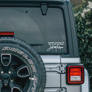 May include: A gray Jeep with a white sticker on the back window that says "Probably listening to the #1 Hot New Band Hot Mulligan".