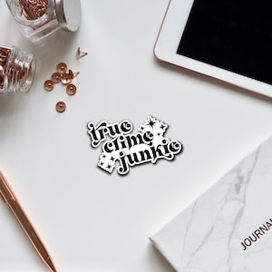 May include: Black and white sticker with the text "true crime junkie" in a retro font with stars around the text.