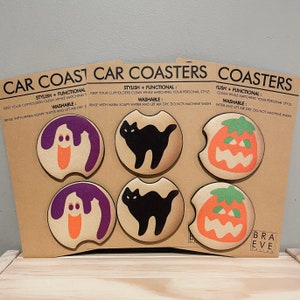 May include: Set of six Halloween-themed car coasters featuring a ghost, a black cat, and a jack-o'-lantern. The coasters are made of a soft, absorbent material and are washable. The text on the coasters reads "Stylish + Functional: Keep your cupholders clean while matching your personal style. Washable: Rinse with warm soapy water and let air dry. Do not machine wash."