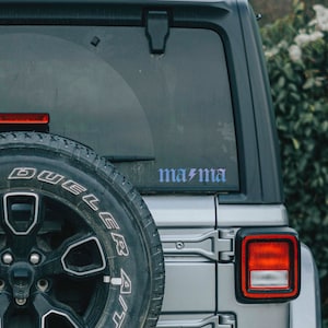 May include: A silver car with a black tire and a sticker that says "ma/ma" on the back window.