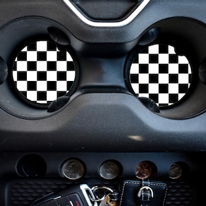 Puede incluir: Insertos de portavasos a cuadros en blanco y negro para un coche. Los insertos son redondos y encajan en los portavasos de la consola central de un coche.
