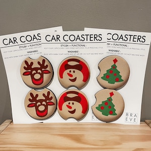 May include: Set of six Christmas-themed car coasters featuring a snowman, reindeer, and Christmas tree designs. The coasters are made of cork and have a brown background with red and green accents. The text on the coasters reads "Stylish + Functional: Keep your cupholders clean while matching your personal style. Washable: Rinse with warm soapy water and let air dry. Do not machine wash."