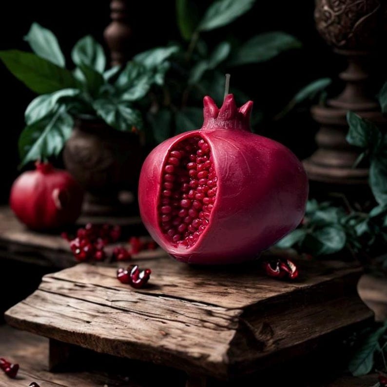 May include: A red pomegranate-shaped candle with a detailed design and a wick. The candle is on a wooden surface with red pomegranate seeds scattered around it.