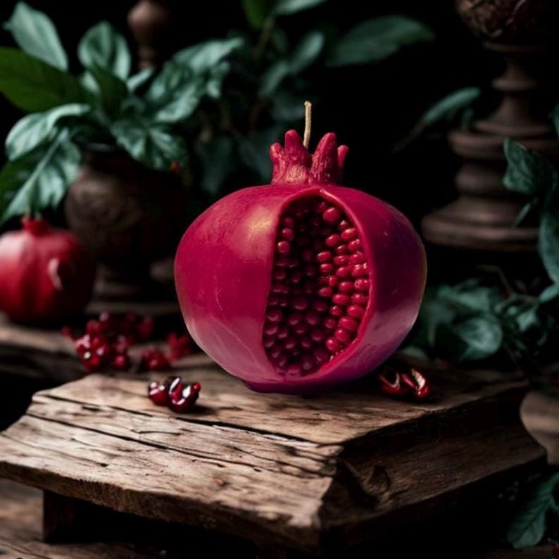 May include: A red pomegranate-shaped candle with a detailed, open design revealing a realistic depiction of the fruit's seeds.