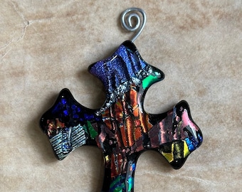 Peut inclure: Une décoration de Noël en forme de croix en verre coloré avec un fil de fer argenté. La croix est composée de nombreux petits morceaux de verre dans des tons de bleu, vert, rouge, orange et jaune.