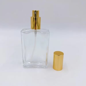 Puede incluir: Una botella de vidrio transparente con un atomizador dorado y una tapa dorada separada. La botella está vacía y lista para ser llenada con tu fragancia favorita.