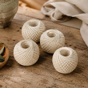 May include: Four spherical balls of off-white twine arranged in a cluster. Each ball features a tightly wound, cross-hatched texture made of thin, natural-colored cord, creating a uniform appearance across all four individual units.