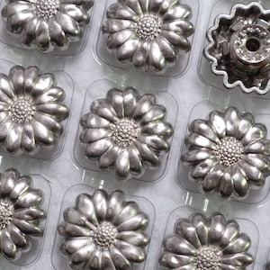 May include: A sheet of silver-colored metal daisy-shaped buttons in a clear plastic packaging. The buttons are arranged in rows and columns.