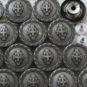 Op de afbeelding: Een set van 12 zilverkleurige metalen knopen met een kruisontwerp. Elke knop heeft een verhoogd kruis in het midden en een decoratieve rand.