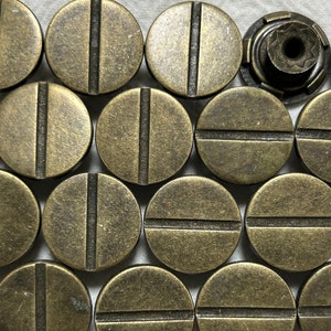 Könnte beinhalten: Eine Sammlung von 13 runden, messingfarbenen Metallknöpfen mit einer einzigen horizontalen Linie in der Mitte jedes Knopfes.