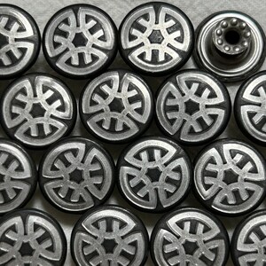 May include: A selection of silver and black metal buttons with a decorative design. The buttons are round with a raised silver pattern on a black background. One button has a different design, with a post for attachment.