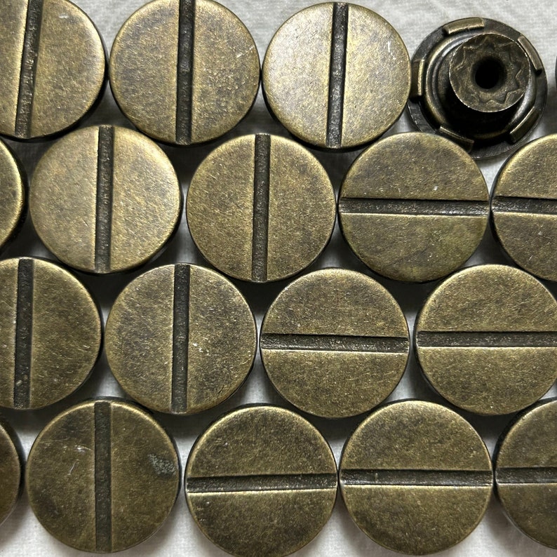 May include: A collection of 13 round, brass-colored metal buttons with a single horizontal line across the center of each button.