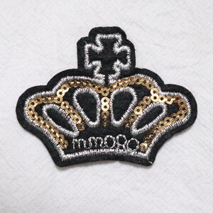 May include: Black felt crown patch with gold sequins and silver embroidery. The crown has a cross on top and the word "moro" embroidered on the bottom.