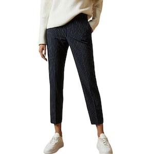 May include: Navy blue pinstripe trousers. The pants have a straight leg cut and are cropped at the ankle. The trousers are paired with white sneakers and a cream-colored sweater.