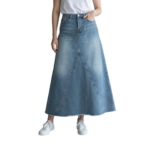 May include: A high-waisted, ankle-length denim skirt in a medium blue wash with a faded finish. The skirt features a button and zipper fly closure, distinct diagonal seam detailing across the front panels, and a raw, frayed hemline at the bottom.
