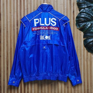 May include: A blue nylon jacket with a white zipper and a white logo that says 'PLUS FORMULA-3000' and 'TEAM TAKE ONE'.