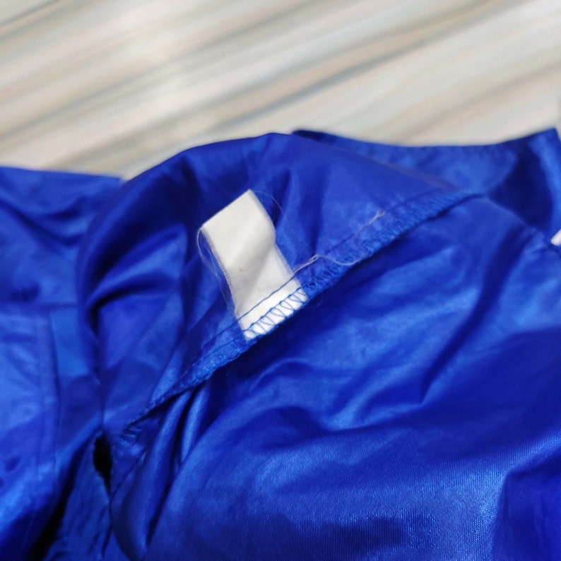 May include: Close up of a blue nylon jacket with a white stripe detail. The jacket is folded and the seam is visible.