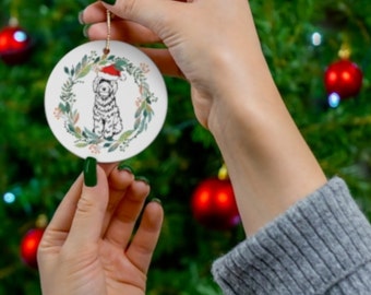 May include: A white ceramic Christmas ornament with a green wreath and a doodle of a dog wearing a Santa hat.