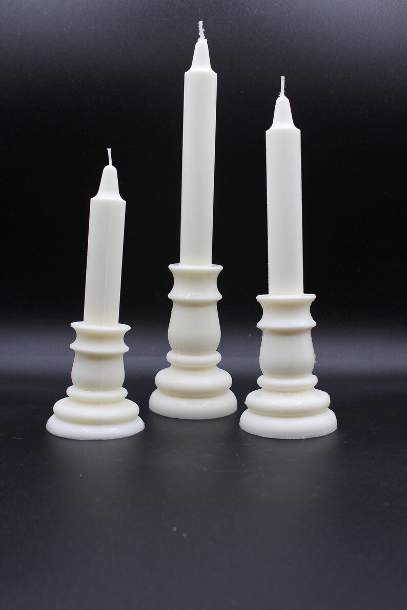 May include: Three white candle holders with white candles. The candle holders are made of ceramic and have a classic design.