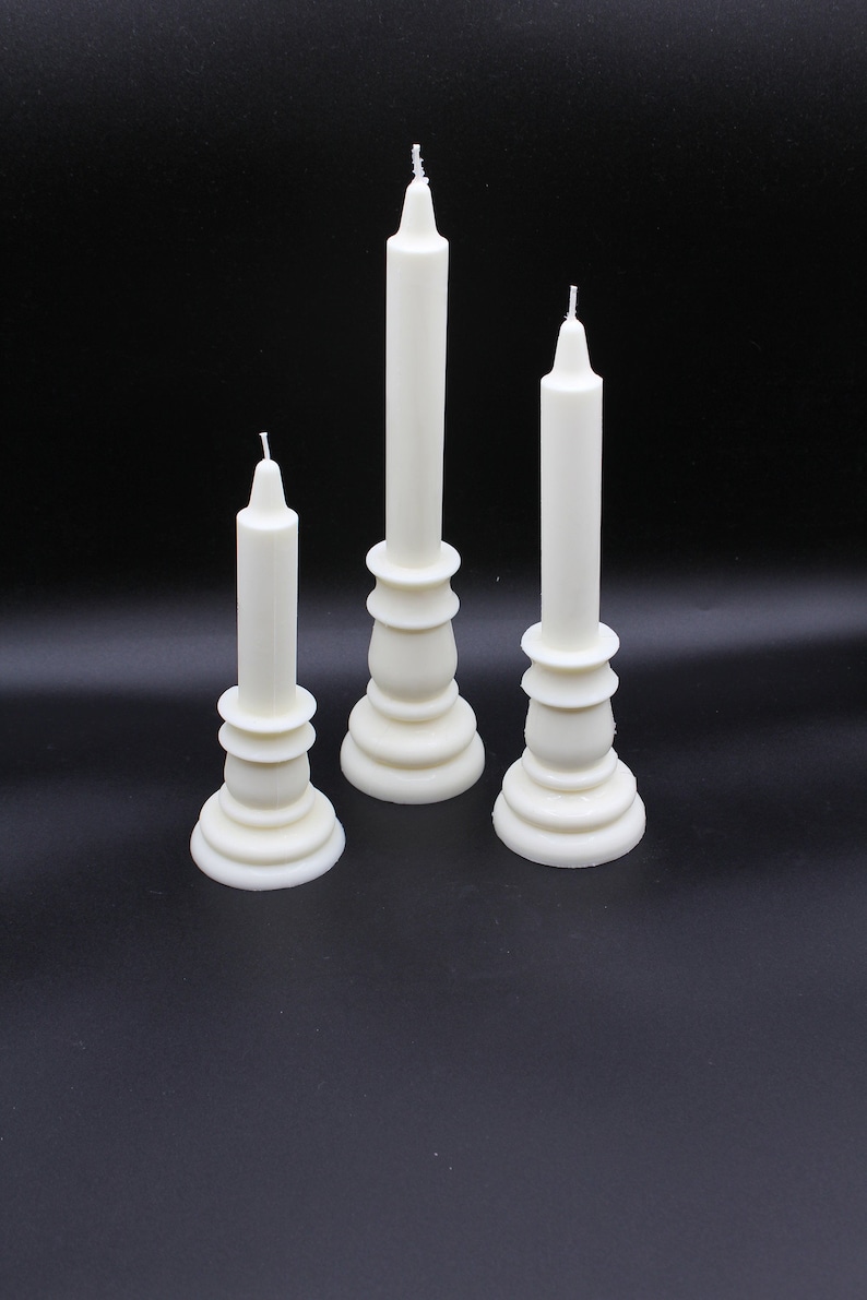 May include: Three white candlesticks with white candles on a black background. The candlesticks are different sizes and have a decorative design.