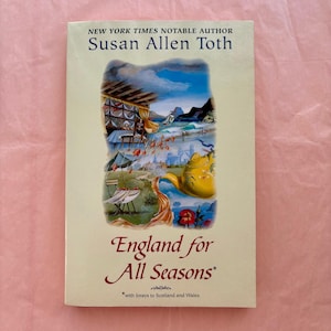 May include: A book titled "England for All Seasons" by Susan Allen Toth. The cover features a colorful illustration of a landscape with a teapot and the text "NEW YORK TIMES NOTABLE AUTHOR". The book is on a pink background.