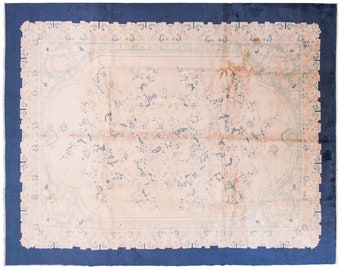 May include: A vintage rug with a light pink background and a blue floral pattern. The rug has a dark blue border.