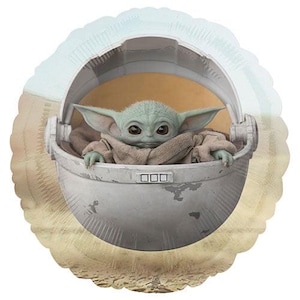 Puede incluir: Un globo de aluminio con el personaje Grogu, tambi&eacute;n conocido como Baby Yoda, de The Mandalorian. El personaje est&aacute; en un portabeb&eacute;s gris con una manta marr&oacute;n claro. El globo tiene un fondo azul claro y beige.