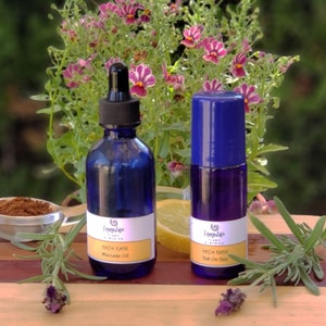 Puede incluir: Dos botellas de vidrio azul con etiquetas que dicen "Pain Ease" y "Roll On Skin". Las botellas están sobre una superficie de madera con una ramita de lavanda y una rodaja de limón.