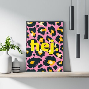 Può includere: Una stampa incorniciata con uno sfondo a stampa leopardata rosa e nera e la parola "hej" in lettere gialle.