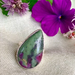 May include: A teardrop-shaped ring with a green and pink gemstone set in silver.