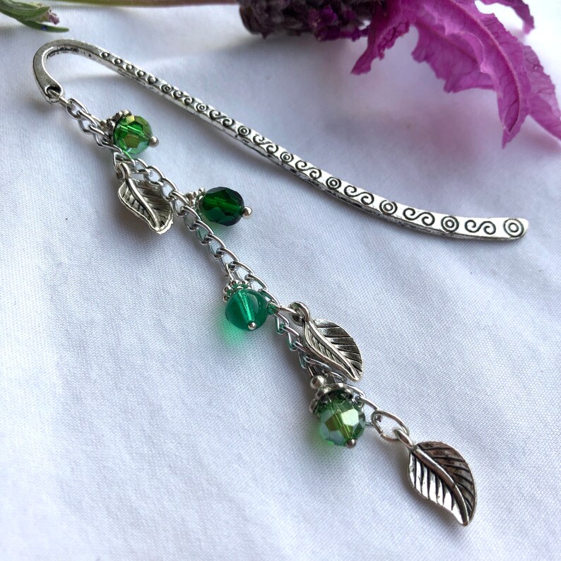 May include: Silver bookmark with a chain and green glass beads. The chain has small silver leaves hanging from it.
