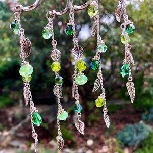 May include: Five silver chains with green glass beads and silver leaf charms. The chains are hanging from a silver hook.