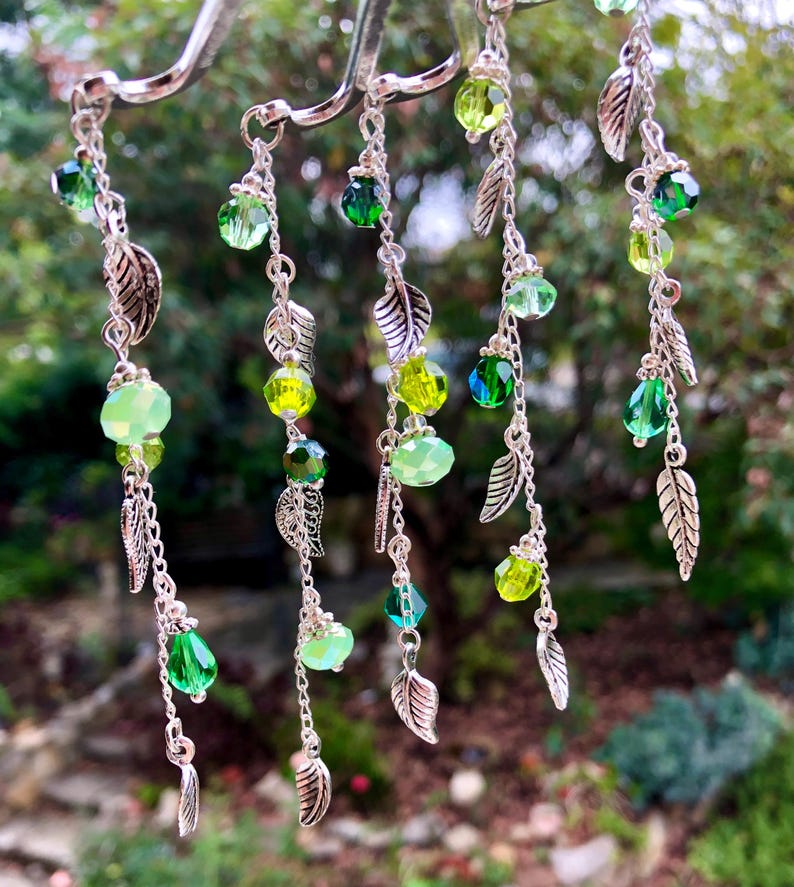 May include: Five silver chains with green glass beads and silver leaf charms. The chains are hanging from a silver hook.