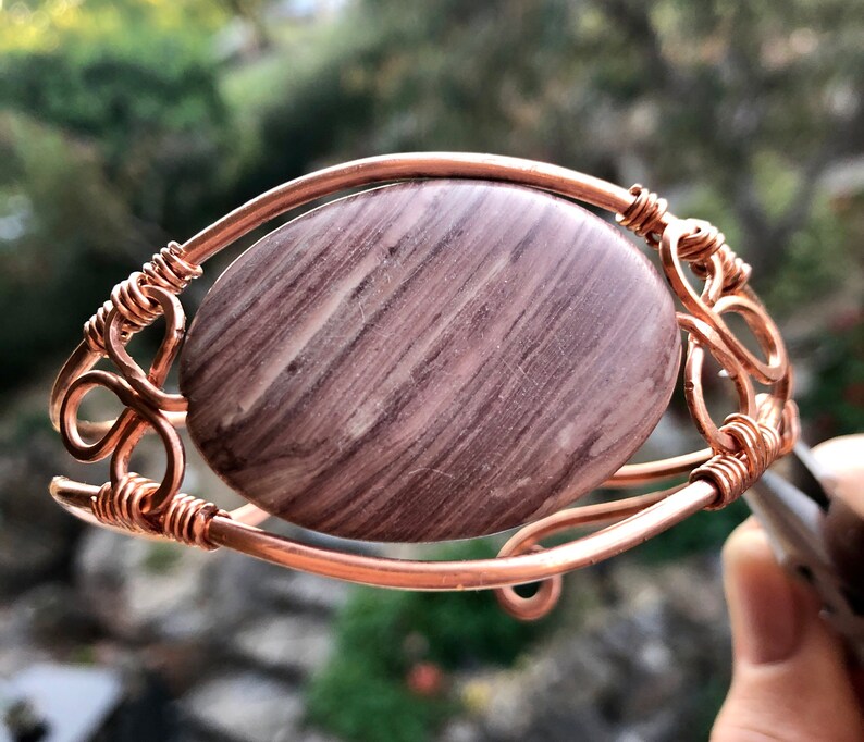 K&ouml;nnte beinhalten: Ein Armband aus Kupferdraht mit einem gro&szlig;en, ovalen, braun-wei&szlig; gestreiften Stein.