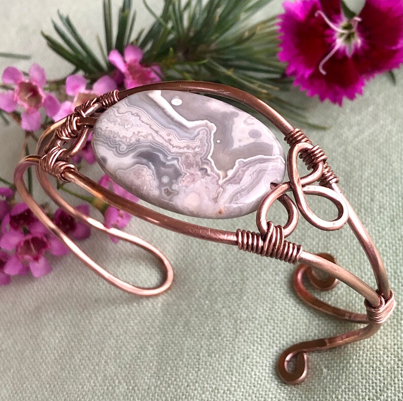 K&ouml;nnte beinhalten: Ein mit Kupferdraht umwickeltes Armband mit einem grauen und wei&szlig;en Achat-Stein. Das Armband hat ein zartes Design mit einem gedrehten Drahtdetail.