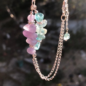 May include: A delicate silver chain necklace with a pendant featuring alternating light blue and lavender gemstone beads.