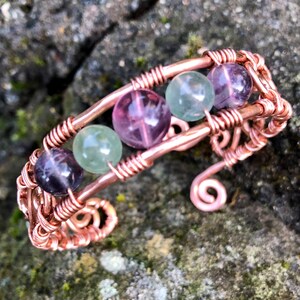 May include: A copper wire wrapped bracelet featuring four fluorite beads. The beads are green, purple, and pink.