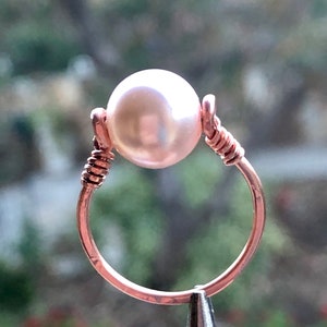 May include: A delicate ring made of rose gold wire with a single white pearl in the centre.