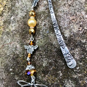 May include: Silver bookmark with a floral design and a dangling charm featuring a bee, beads, and a dragonfly.